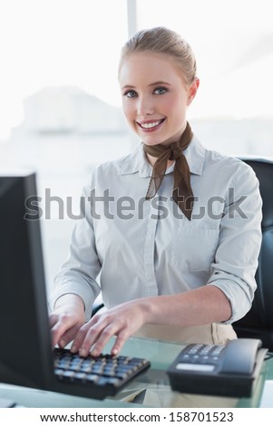 Blonde smiling businesswoman working on computer in bright office