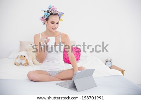 Concentrated natural brown haired woman in hair curlers using a tablet pc in bright bedroom
