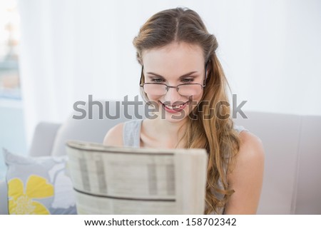 Happy young woman sitting on sofa reading newspaper at home in the sitting room
