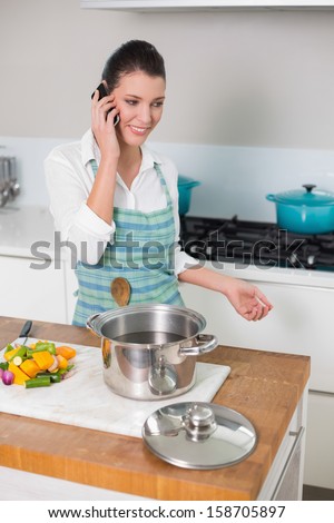 Cheerful pretty woman wearing apron having a call in bright kitchen