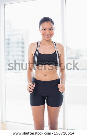 Content dark haired model in sportswear holding a skipping rope in bright fitness studio
