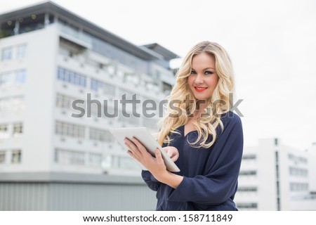 Smiling gorgeous blonde with red lips using tablet on urban background