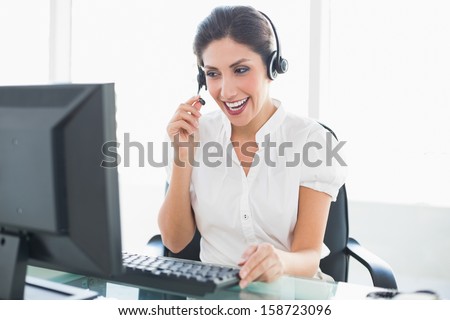Laughing call center agent sitting at her desk on a call in her office