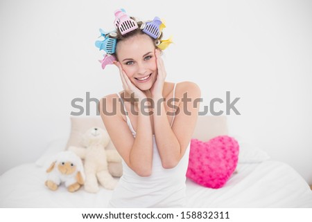 Relaxed natural brown haired woman in hair curlers touching her face in bright bedroom