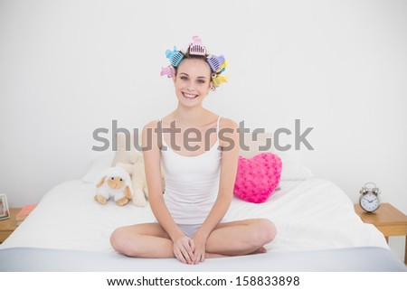 Smiling natural brown haired woman in hair curlers practicing yoga in bright bedroom