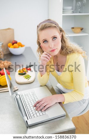 Day dreaming cute blonde using laptop in bright kitchen