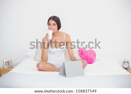Relaxed young brown haired model in white pajamas drinking milk in bright bedroom
