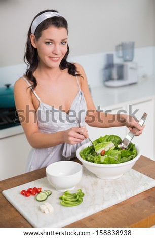 Smiling pretty brunette mixing healthy salad in bright kitchen