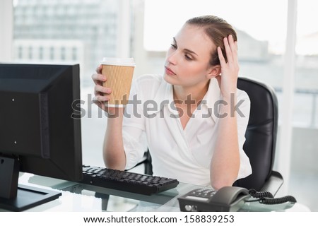 Tired businesswoman holding disposable cup sitting at desk in her office