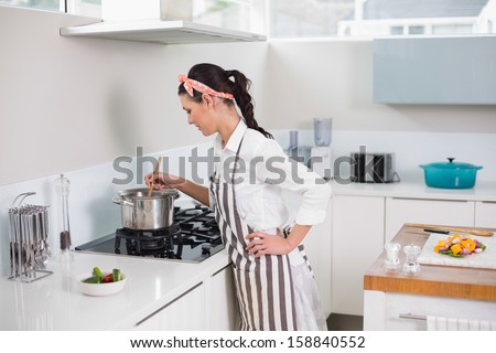 Concentrated pretty woman with apron cooking in bright kitchen