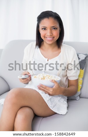 Lovely young dark haired woman in white clothes watching tv in a living room
