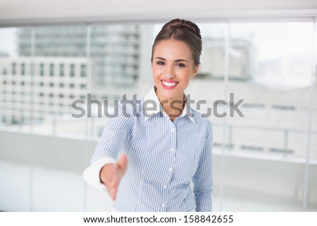 Cheerful brunette businesswoman standing for hand shake in bright office