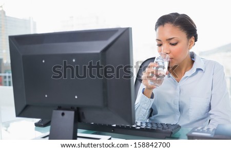 Relaxed young dark haired businesswoman drinking water in bright office
