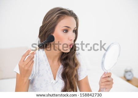 Attractive young brunette holding a brush and a mirror in bright bedroom