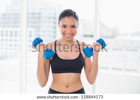 Motivated dark haired model in sportswear exercising with dumbbells in bright fitness studio