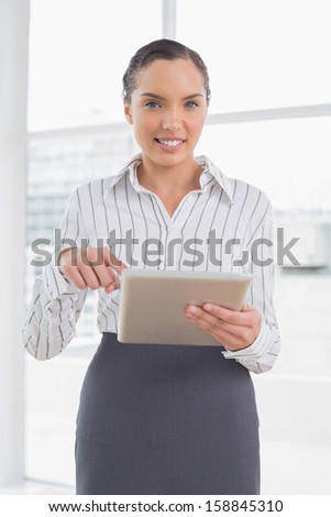 Businesswoman standing in her office and pointing at tablet screen while looking at camera