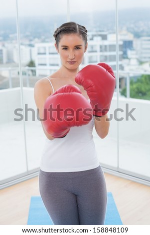 Competitive sporty brunette wearing red boxing gloves in bright fitness studio