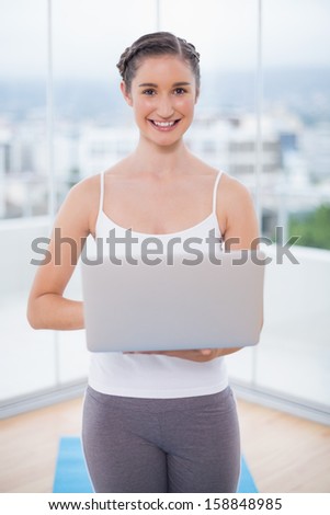 Cheerful sporty brunette using her laptop in bright fitness studio
