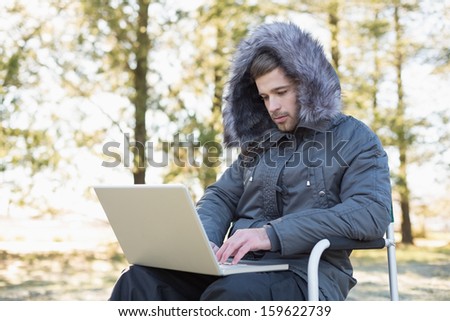 Young man in warm clothing using laptop in the forest on a winter day