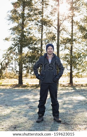 Full length portrait of a young man in warm clothing while having a walk in forest on a winter day