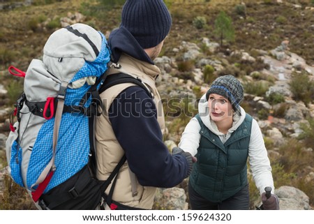 Man helping a woman to climb up rock on a hike