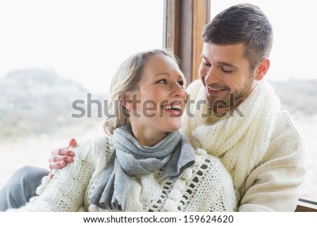 Cheerful young couple in winter clothing against cabin window