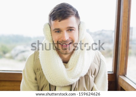 Portrait of a smiling young man wearing earmuff while sitting against cabin window