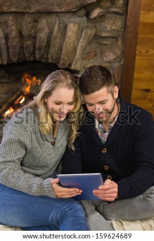 Happy lovely young couple using tablet PC in front of lit fireplace