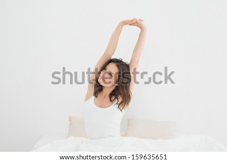 Young woman waking up in bed and stretching her arms