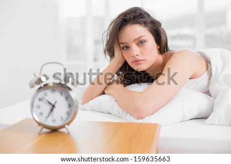 Portrait of a beautiful young woman lying in bed with alarm clock on bedside table