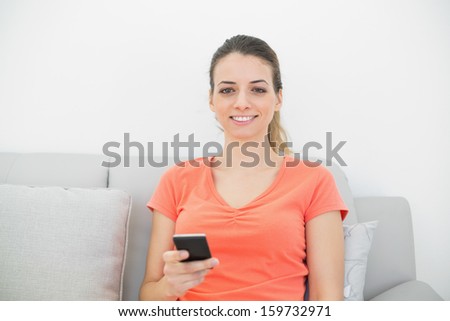 Casual calm woman holding her smartphone sitting on couch smiling at camera