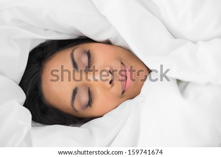 Lovely smiling woman lying on bed under cover with eyes closed