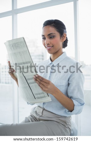 Lovely smiling calm businesswoman reading newspaper sitting in bright office