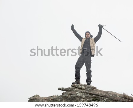 Full length low angle view of a man with hands raised on rock against the sky