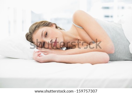Beautiful tired woman lying in her bed under the cover looking peacefully at camera