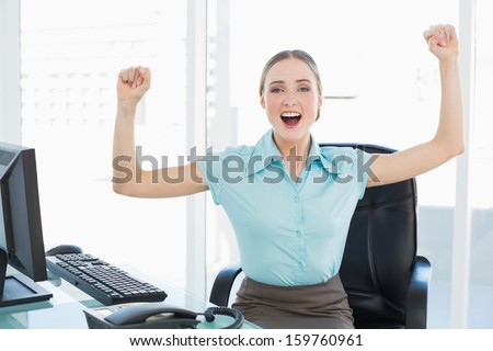 Classy cheerful businesswoman cheering with raised arms in bright office