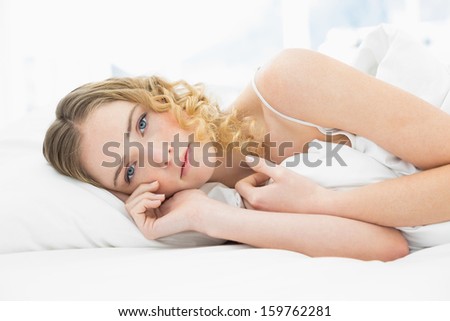 Pretty unsmiling blonde lying in bed resting in bright bedroom