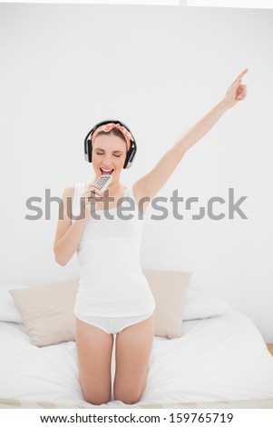 Young woman pretending to sing while listening to music with closed eyes and raising an arm