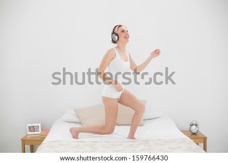 Laughing woman playing air guitar while listening to music and standing on her bed