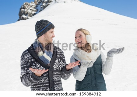 Young couple in warm clothing with hands open looking at each other in front of snowed hill