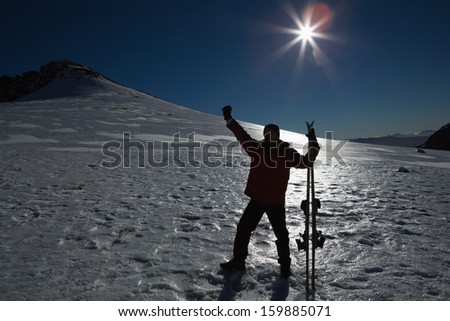 Silhouette man raising hand with ski board on snow covered landscape against clear blue sky