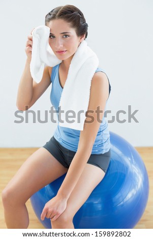 Portrait of a young woman with towel around neck sitting on exercise ball