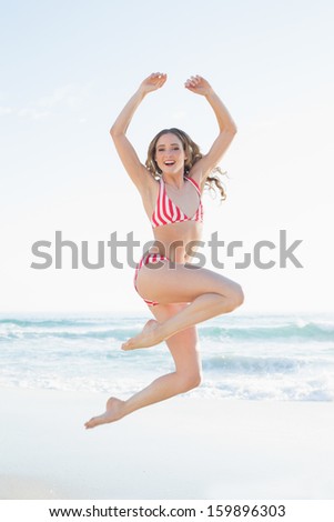 Young woman jumping on the beach wearing a red bikini smiling at camera