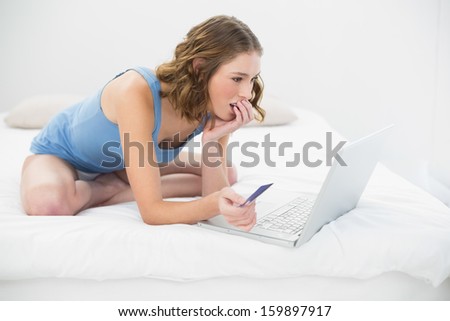Concentrated pretty woman using her notebook for home shopping sitting on her bed