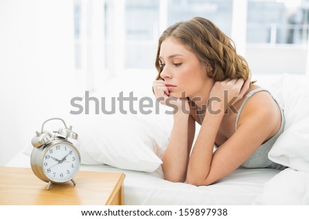 Young woman lying in her bed looking at the alarm clock in her bedroom