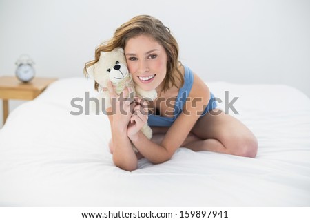 Happy woman posing with her white teddy bear sitting on bed smiling at camera