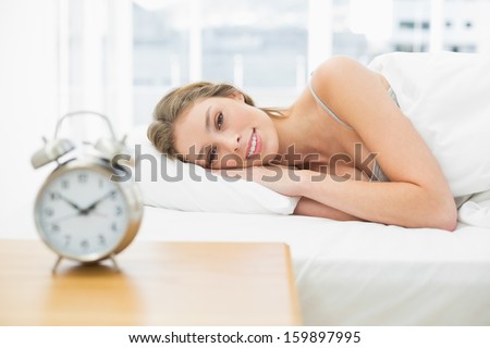 Beautiful calm woman lying in her bed under the cover smiling at camera