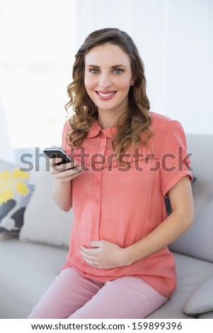 Content calm pregnant woman holding her smartphone sitting on couch smiling at camera