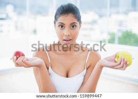 Astonished toned brunette holding apples in bright room