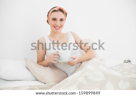 Smiling woman holding a cup of tea lying in her bed in the bedroom